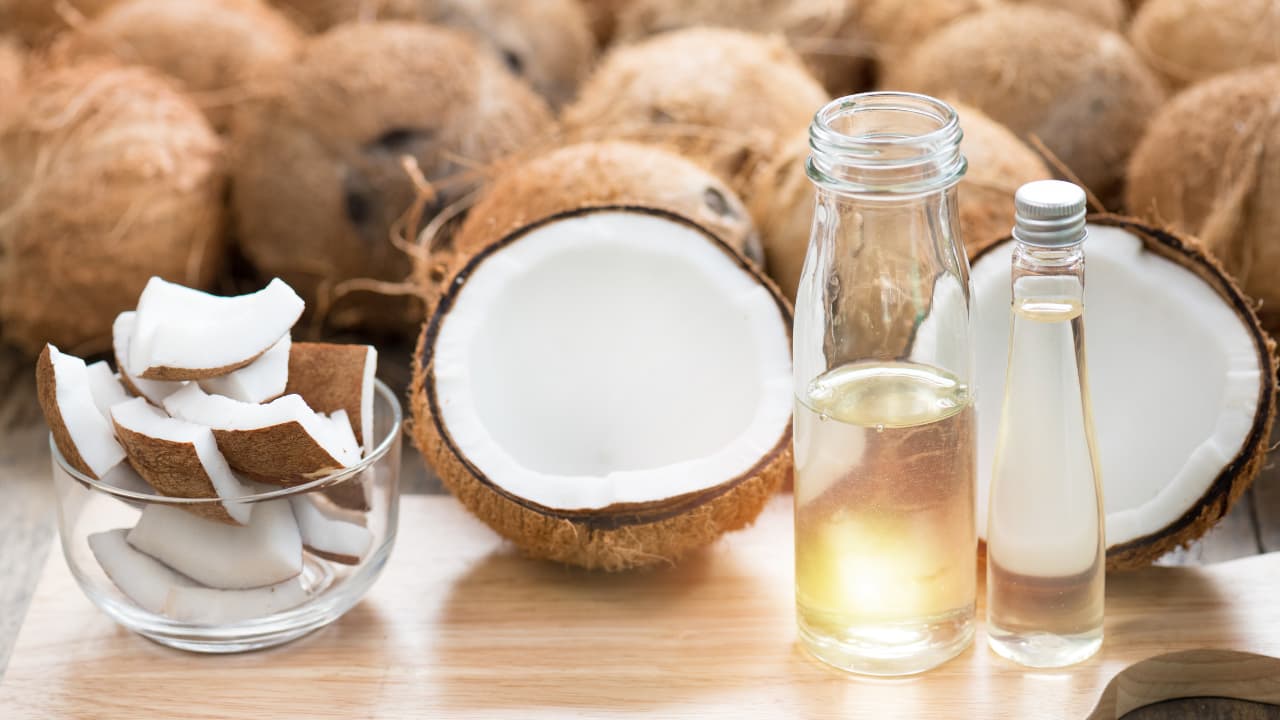 Bottle of coconut oil surrounded by coconuts